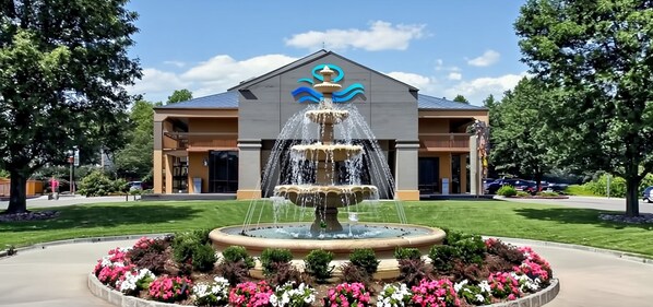 A building with a fountain and flower beds in front.