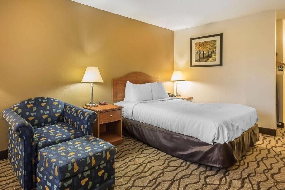 A hotel room with a bed, two bedside lamps, a chair, and a nightstand.