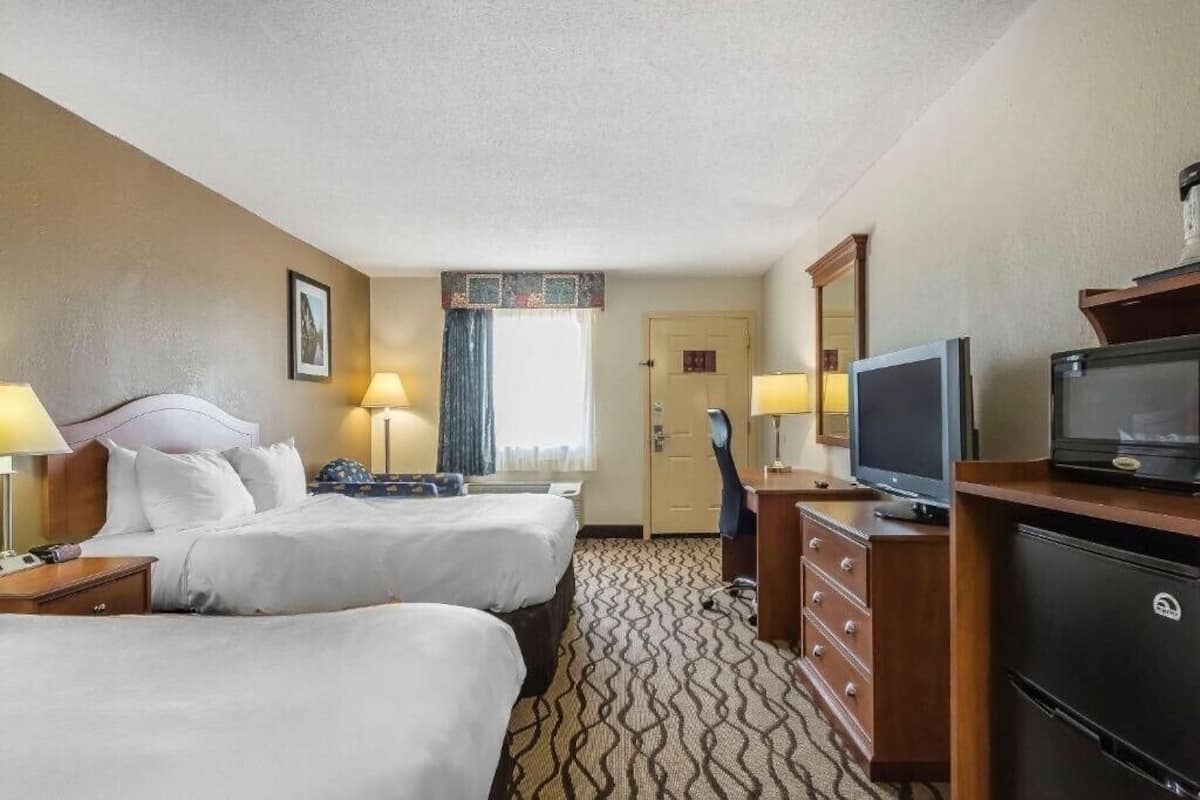 A hotel room with two beds, a television, a desk with a chair, and a minibar.