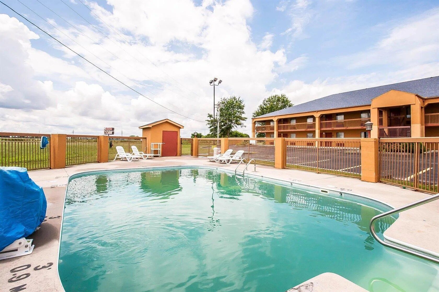 A swimming pool with lounge chairs and a fenced area, surrounded by a building with multiple balconies.
