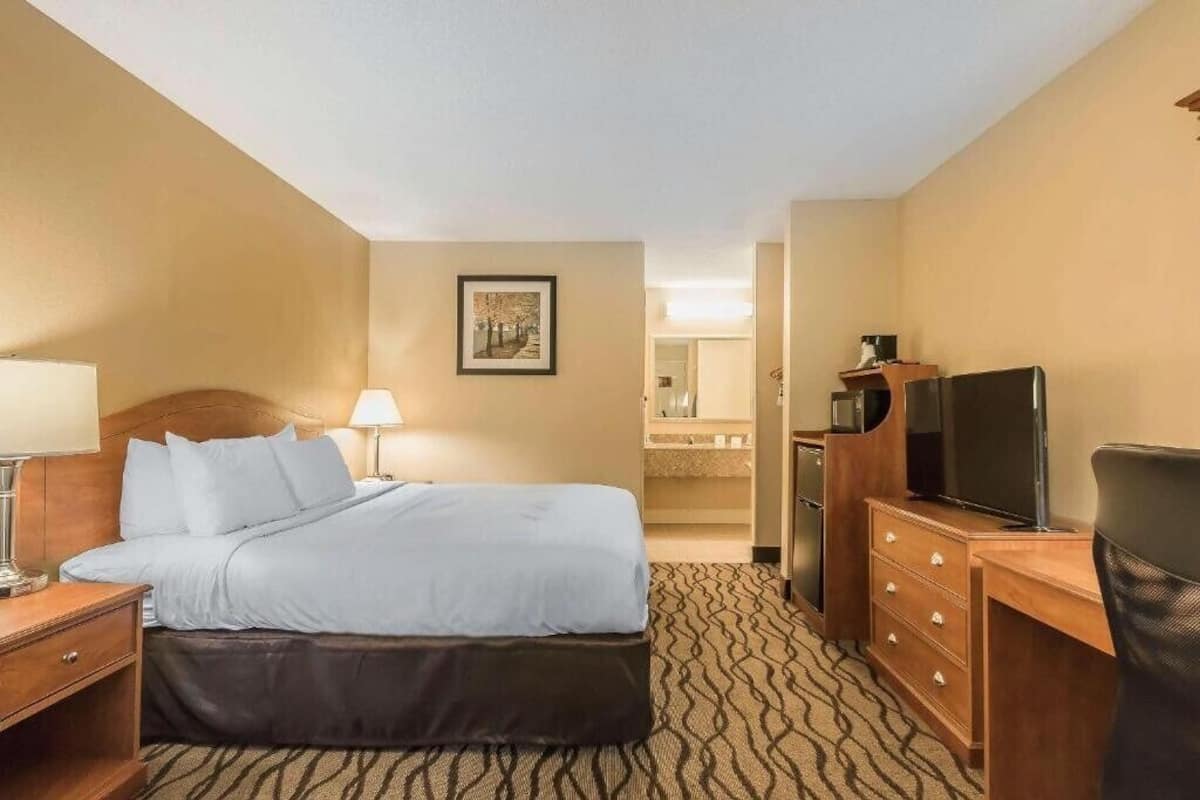 A hotel room with a bed, a desk, a television, and a bathroom visible in the background.