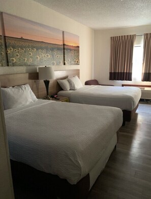 A hotel room with two beds, a painting on the wall, a lamp, and a window with curtains. - Days Inn by Wyndham Topeka (Topeka)