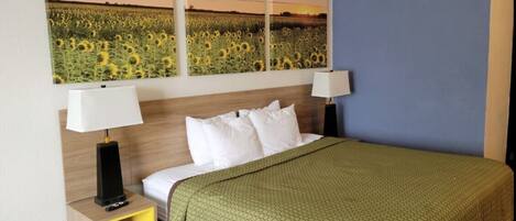 A hotel room with a bed, two bedside tables, a green bedspread, and three wall-mounted paintings of a sunflower field.