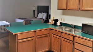 Una cocina compacta con armarios de madera, encimera verde, lavamanos y refrigerador negro.