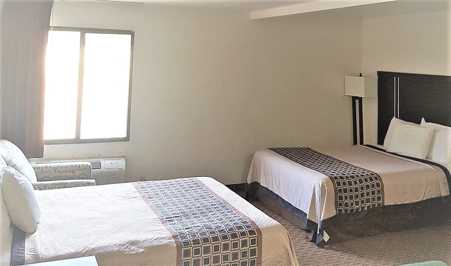A hotel room with two beds, a window, and a bedside lamp.