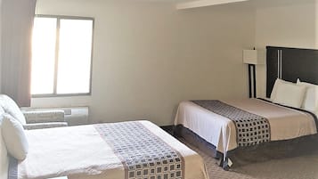 A hotel room with two beds, a window, and a bedside lamp.
