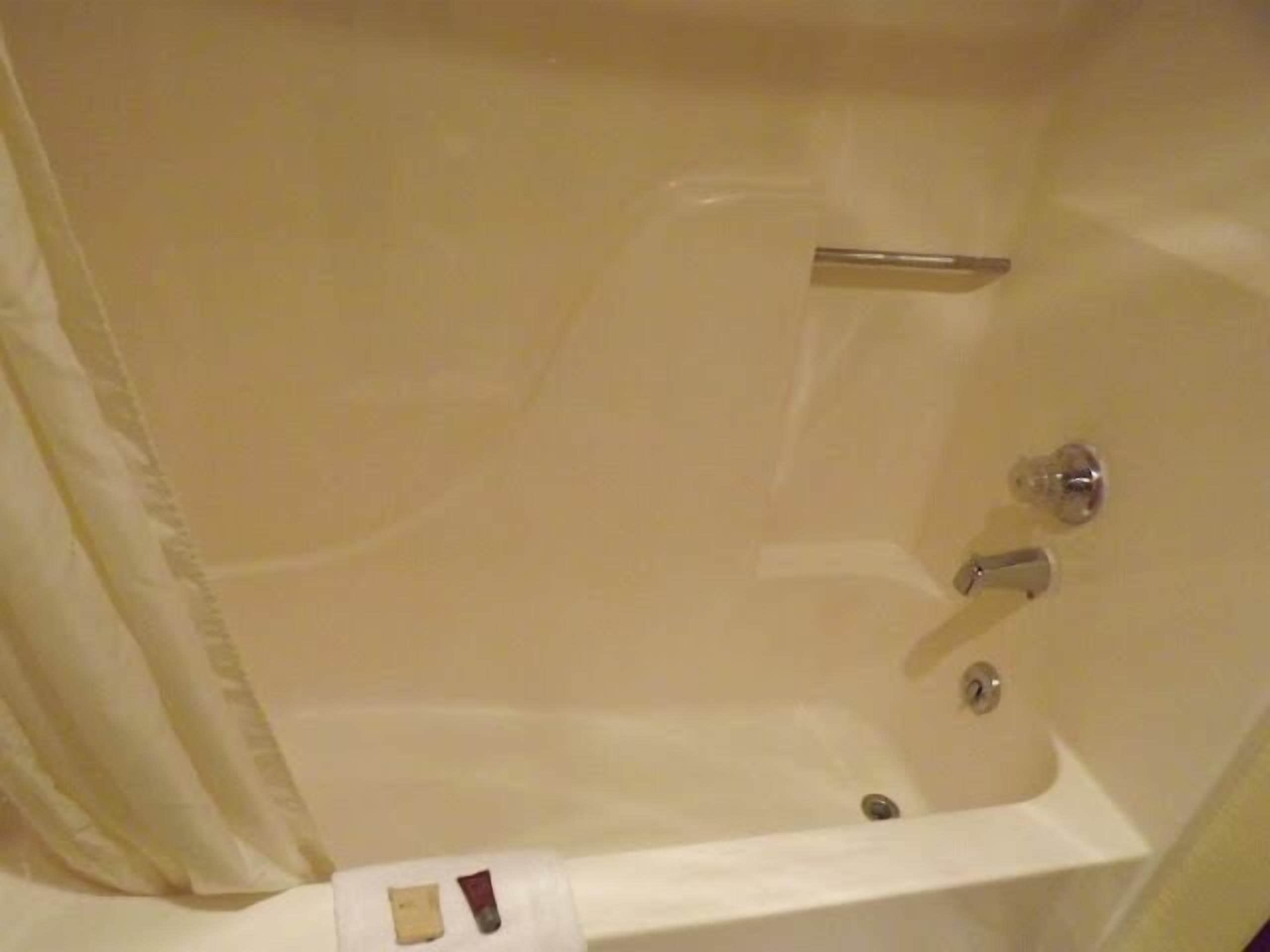 A bathtub with a shower curtain, a handheld showerhead, and a handheld massager.