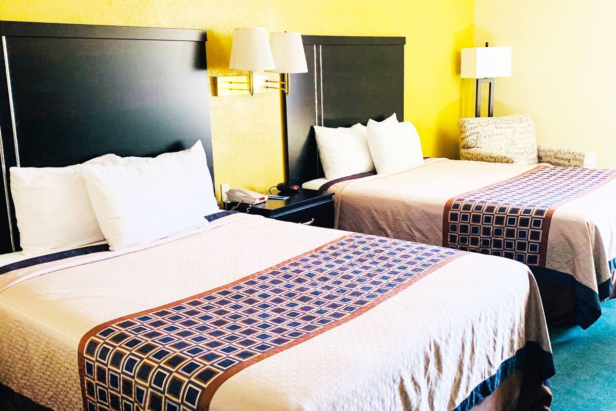 A hotel room with two beds, each with a headboard, bedside lamps, and a patterned bedspread.