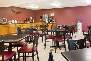 A restaurant with multiple tables and chairs, a counter with various appliances, and a water dispenser.