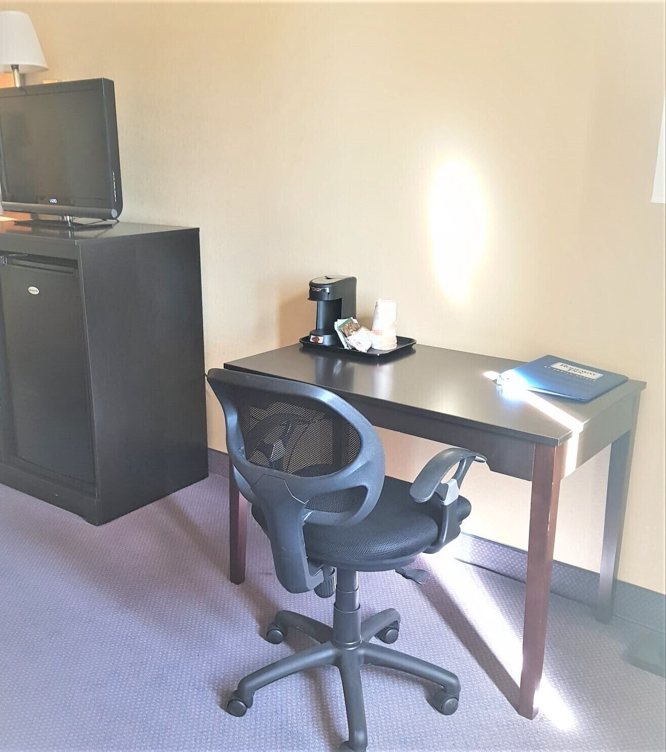 A hotel room with a desk, office chair, coffee maker, and a television on a cabinet.
