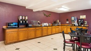 Una barra de desayuno con armarios de madera, un microondas, máquinas de café y un área de estar con sillas.