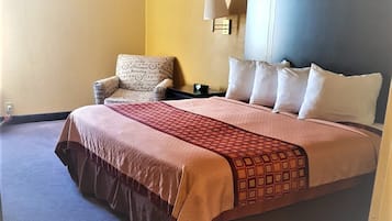 A hotel room with a large bed, a chair, a nightstand, and a wall-mounted lamp.
