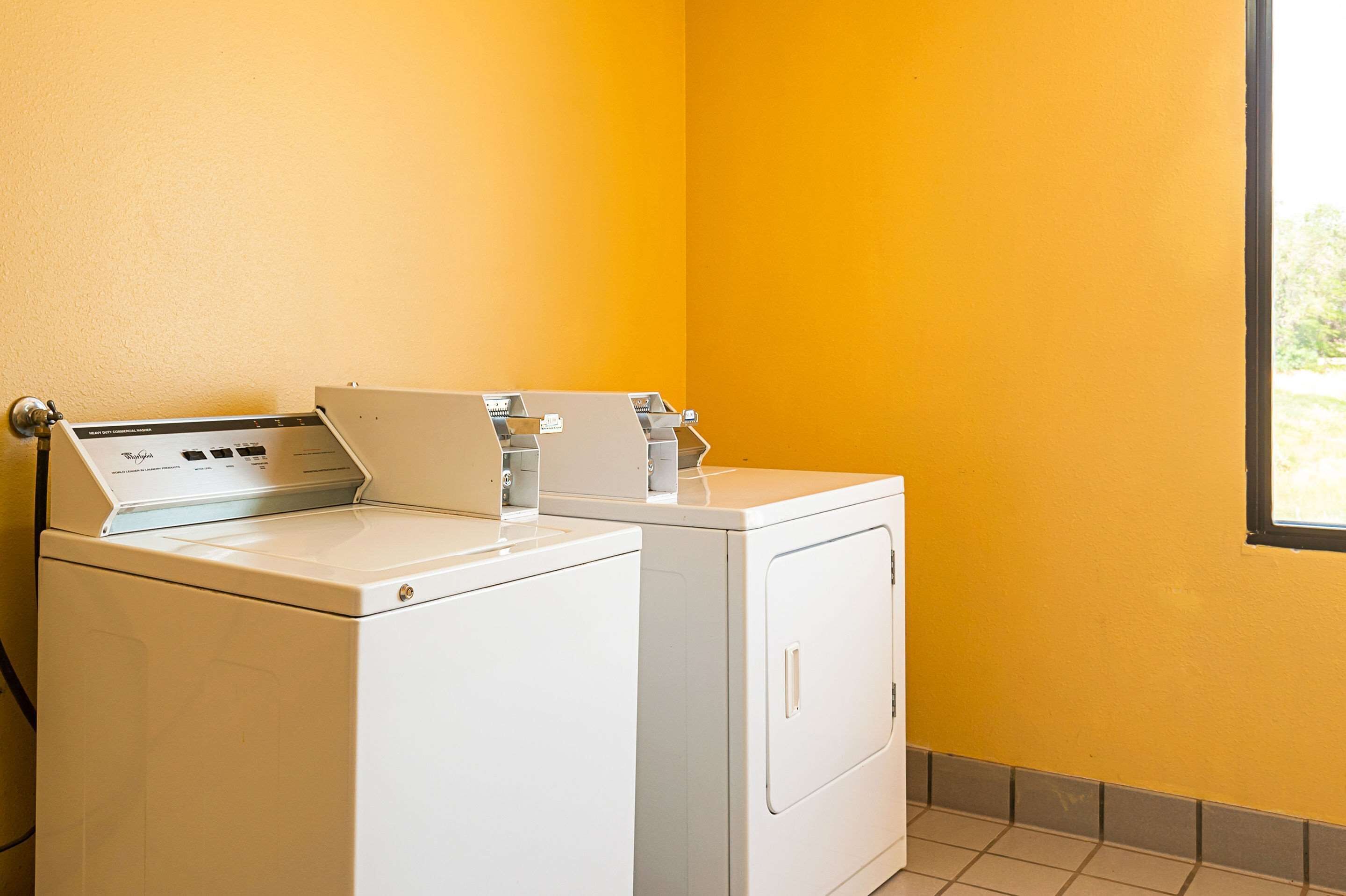 A laundry room with two white washing machines and a dryer, a yellow wall, and a window.