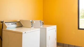 A laundry room with two white washing machines and a dryer, a yellow wall, and a window.