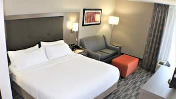 A hotel room with a large bed, a desk, a chair, and a small ottoman.
