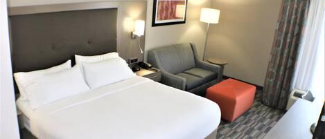A hotel room with a large bed, a desk, a chair, and a small ottoman.