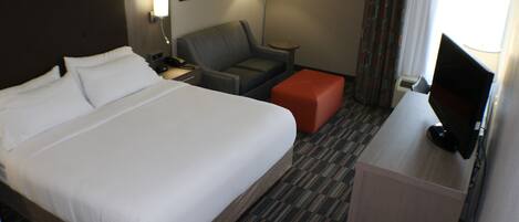 A hotel room with a large bed, a desk with a television, a chair, and a small table.