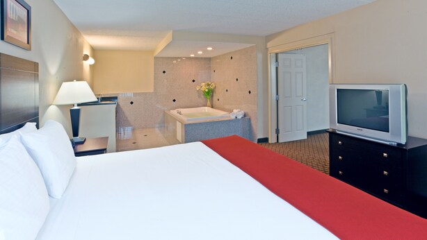 Habitación de hotel con cama, televisor, escritorio con lámpara y baño con bañera.