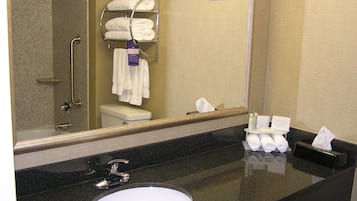 A bathroom with a black countertop, a white sink, a mirror, a towel rack with folded towels, and a toilet.