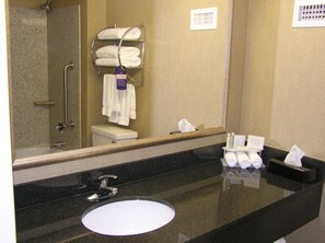 A bathroom with a black countertop, a white sink, a mirror, a towel rack with folded towels, and a toilet.