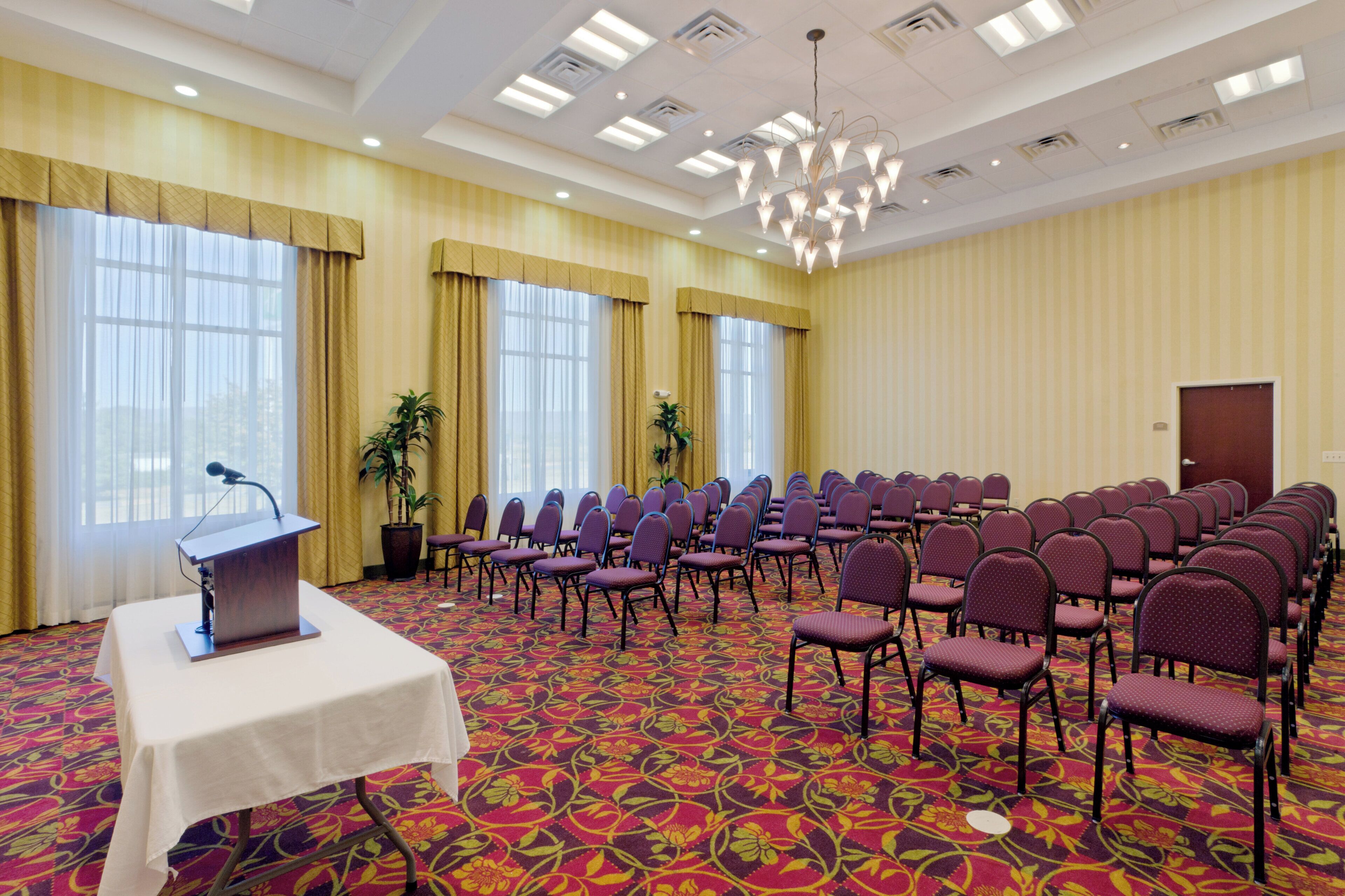 A conference room with rows of chairs, a podium, and large windows with curtains.