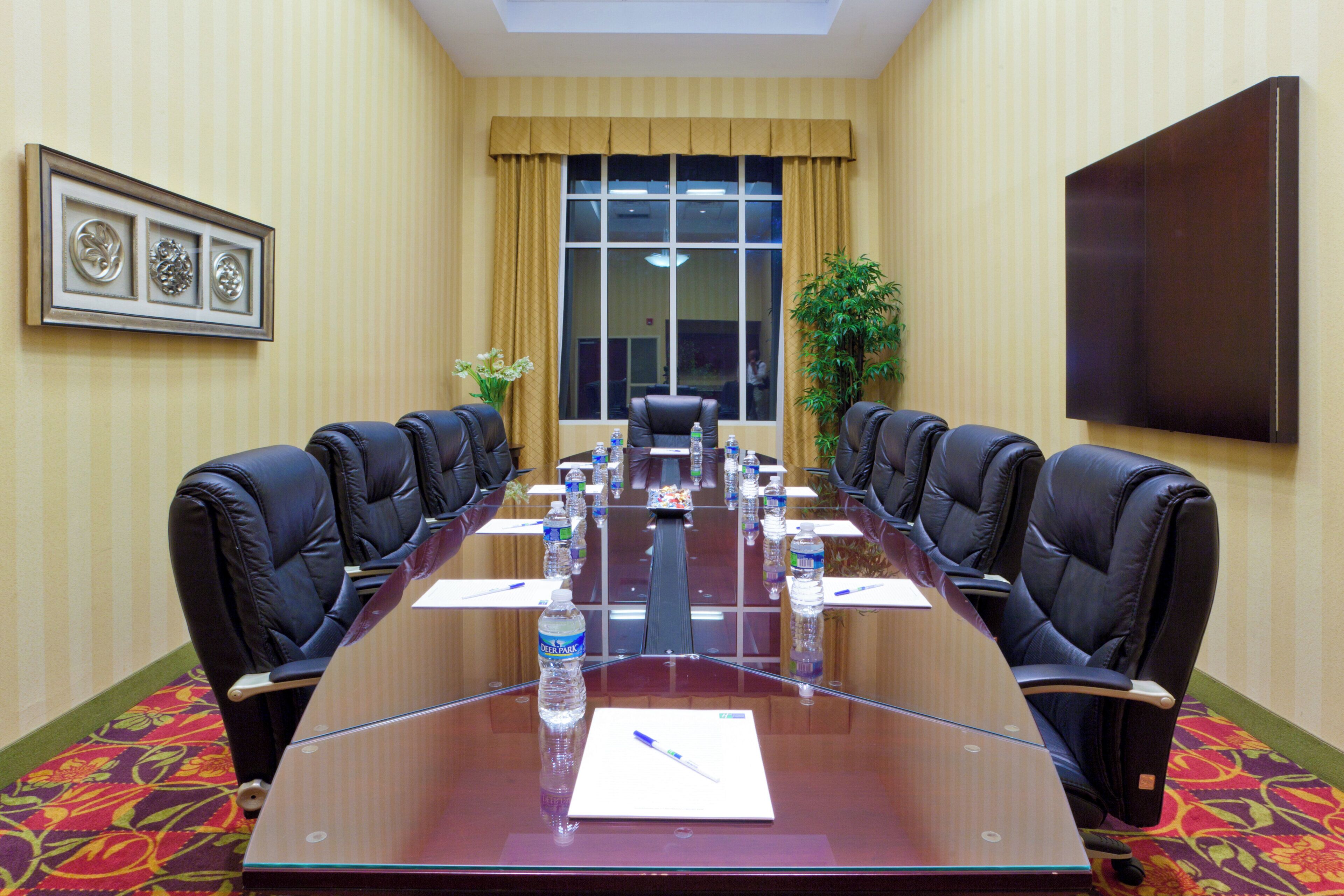 A conference room with a long table, chairs, water bottles, and a plant.