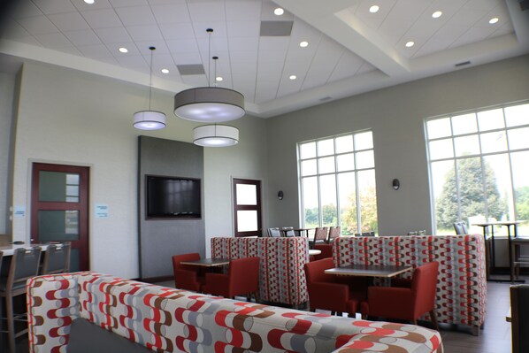 A dining area with booths and tables, large windows, and ceiling lights.
