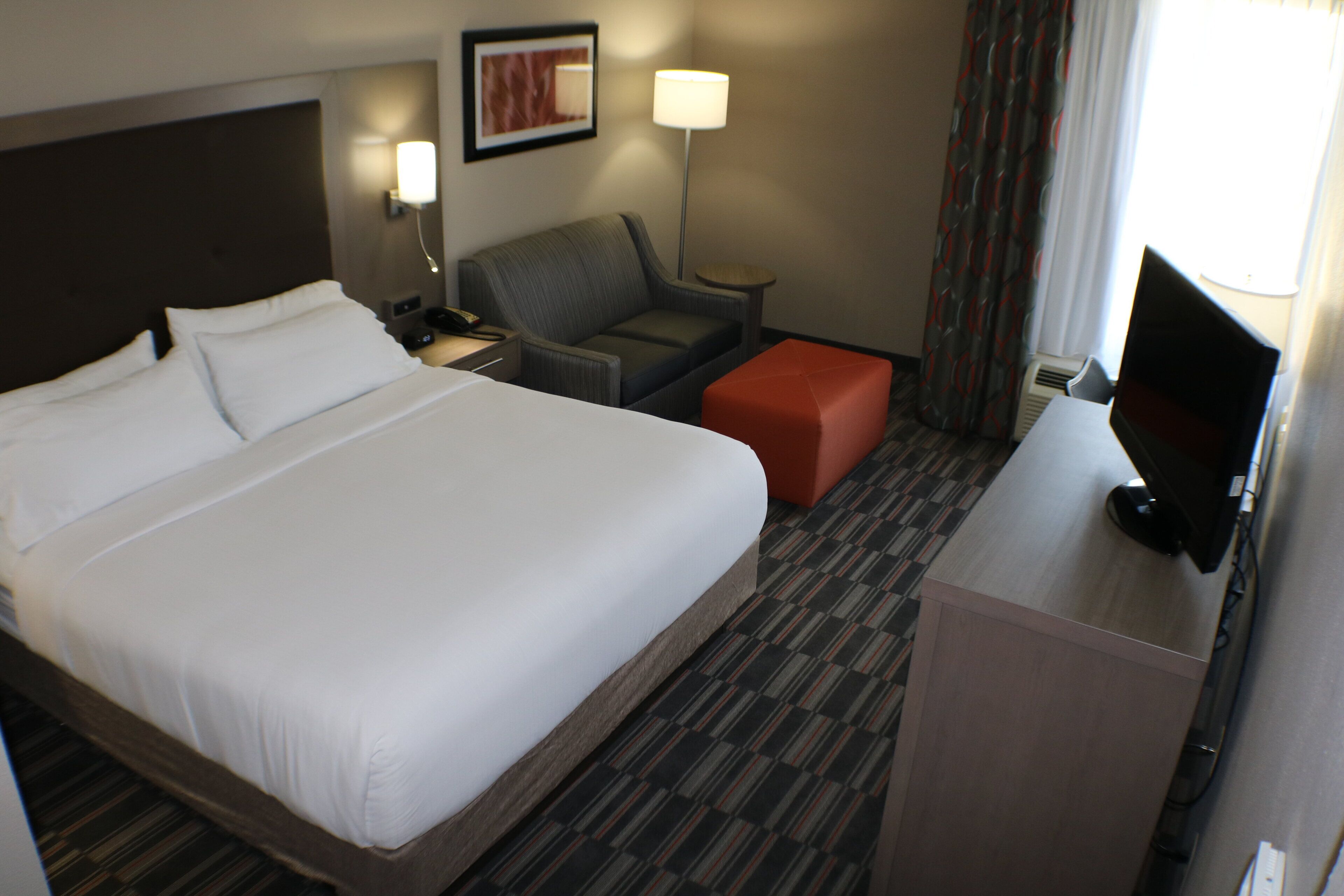 A hotel room with a large bed, a desk, a chair, a TV, and a small table.