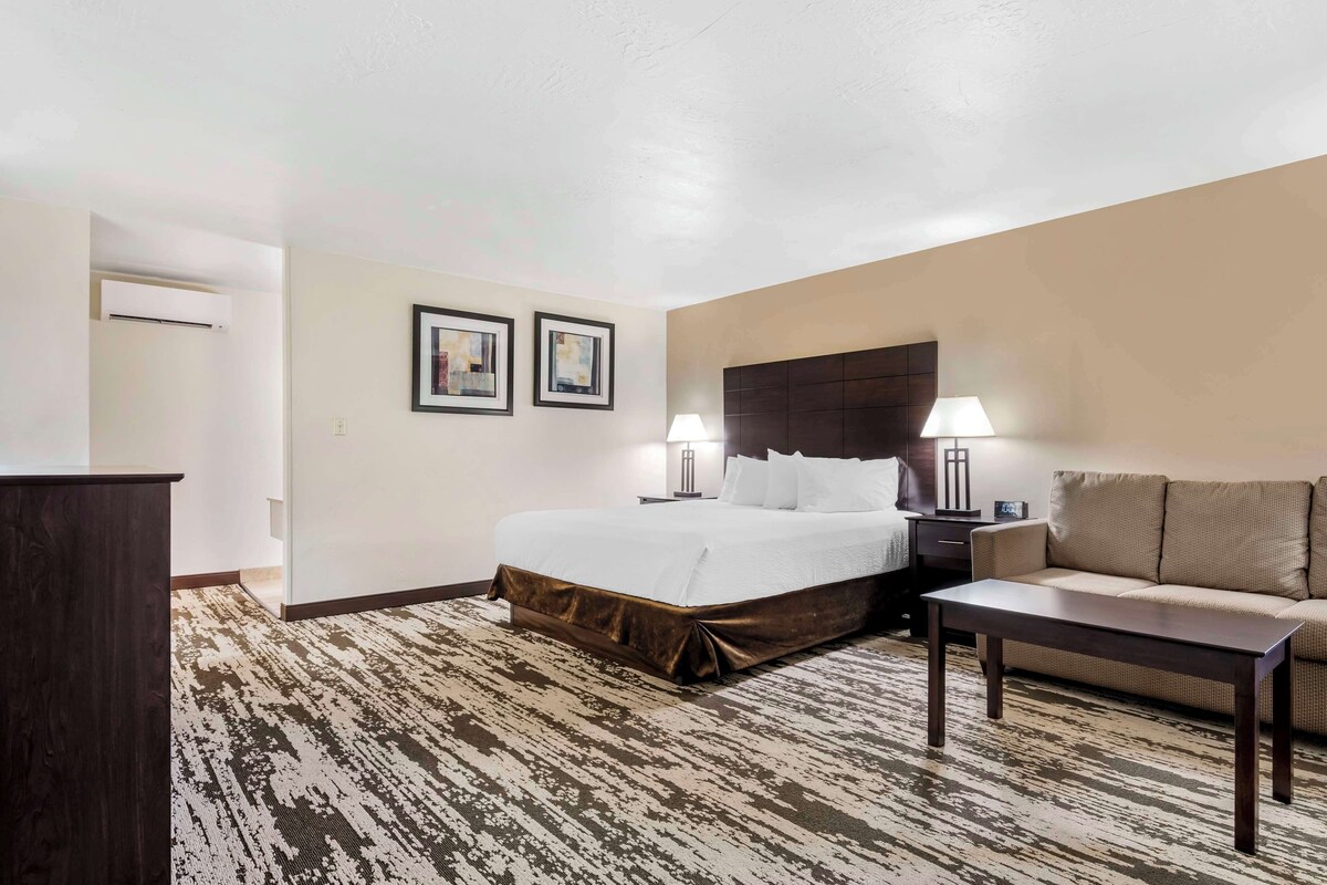 A hotel room with a bed, a sofa, a table, and two wall-mounted lamps.