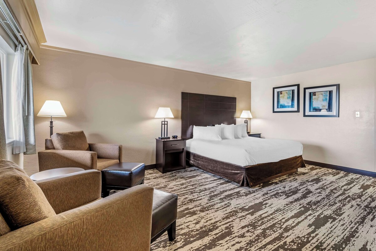 A hotel room with a large bed, two bedside tables with lamps, a sofa, and a small table.