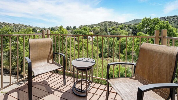 A balcony with two wicker chairs and a small round table, overlooking a lush green landscape with hills. - Best Western Prescottonian (Prescott)