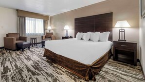 A hotel room with a large bed, two armchairs, a small table, and a nightstand with a lamp. - Best Western Prescottonian (Prescott)