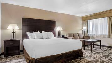 A hotel room with a large bed, two bedside tables with lamps, a sofa, a small table, and a window with curtains.