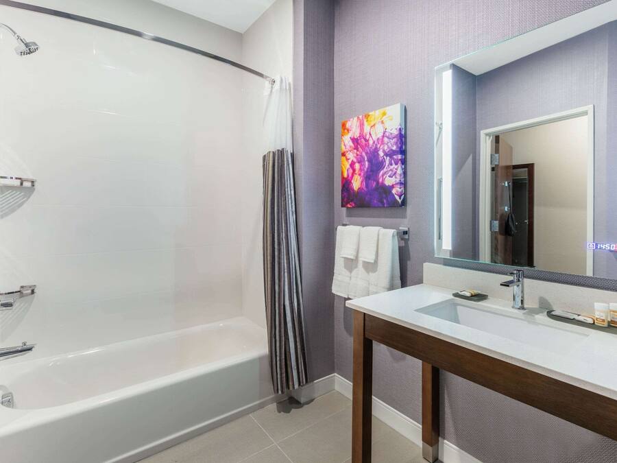 A modern bathroom with a bathtub, a vanity with a mirror, and a colorful abstract painting on the wall.