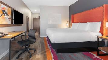A hotel room with a bed, desk, chair, TV, and a motivational poster on the wall.