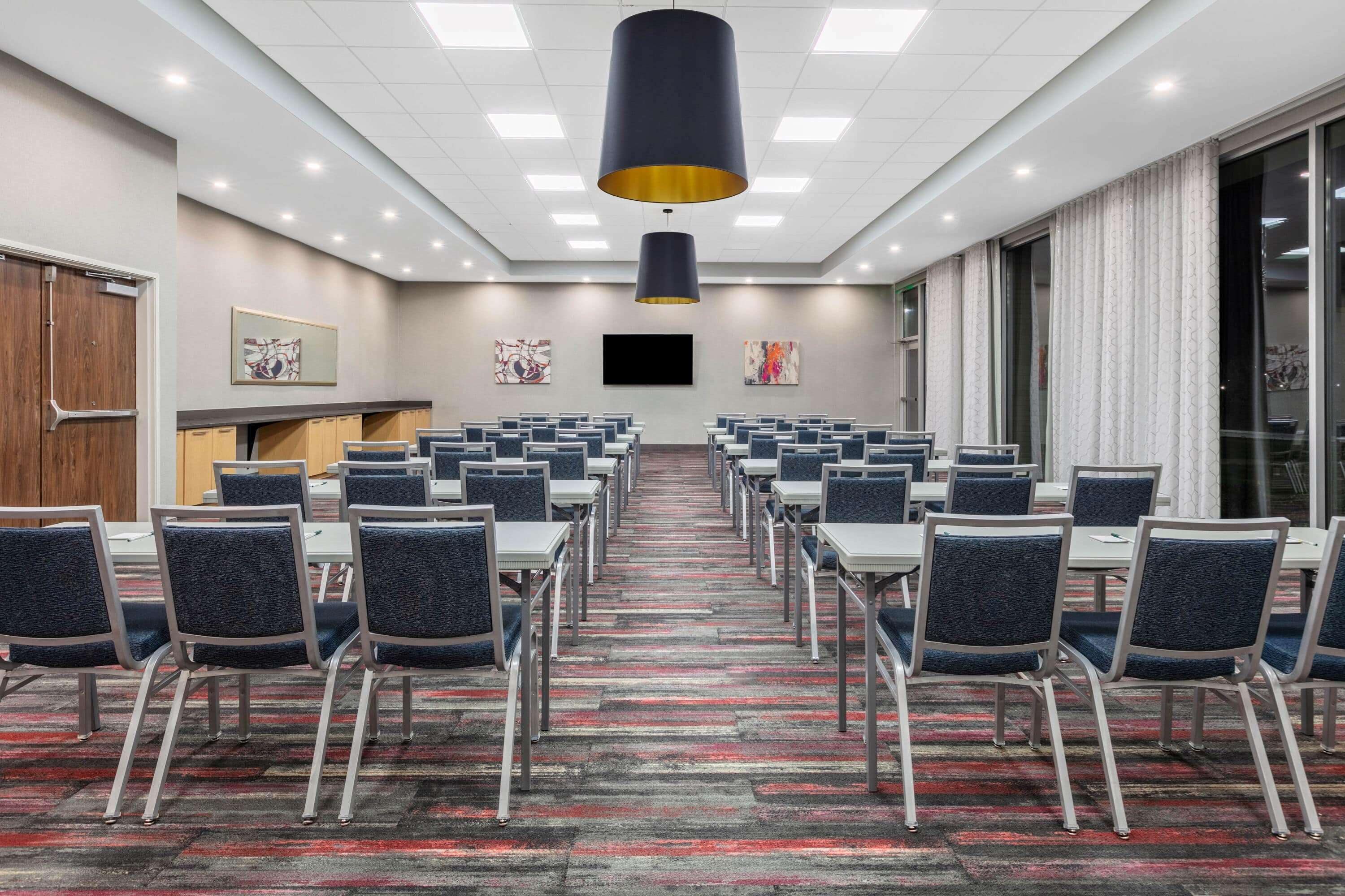 A conference room with rows of tables and chairs, a large black pendant light, and artwork on the walls.