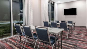 Un salón de conferencias con mesas y sillas, una televisión de pantalla plana y amplias ventanas con cortinas.