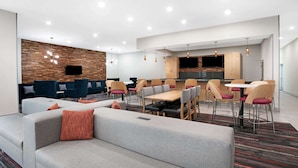 A modern hotel lobby with a seating area, a dining table, and a kitchen area. - La Quinta Inn & Suites by Wyndham Lewisville (Lewisville)