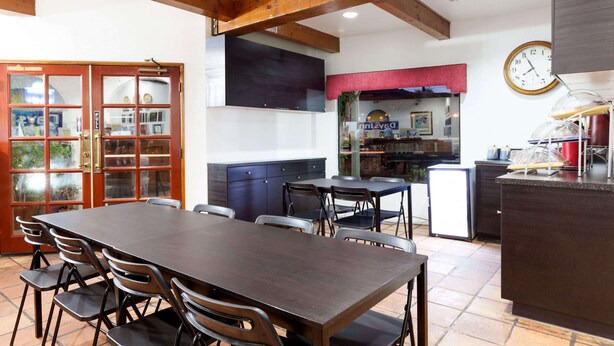 A dining area with a large table and chairs, a kitchen area with a refrigerator, and a clock on the wall. - Days Inn by Wyndham Castaic Six Flags Magic Mountain (Castaic)