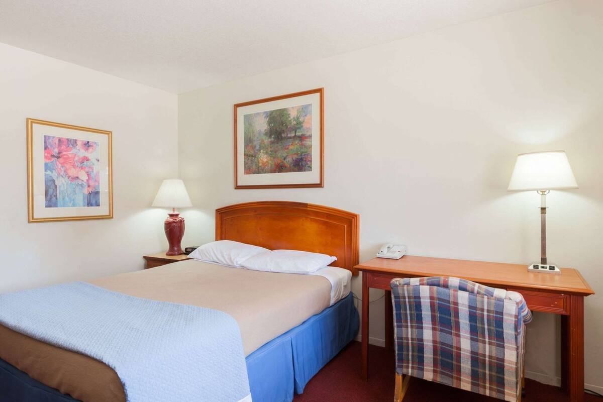 Ein Hotelzimmer mit einem Bett, einem Schreibtisch, zwei Lampen und zwei gerahmten Bildern an den Wänden.