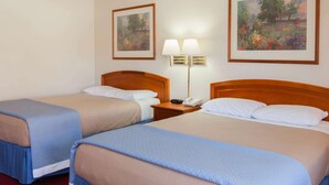 A hotel room with two beds, a nightstand with a lamp, and two framed paintings on the walls. - Days Inn by Wyndham Castaic Six Flags Magic Mountain (Castaic)