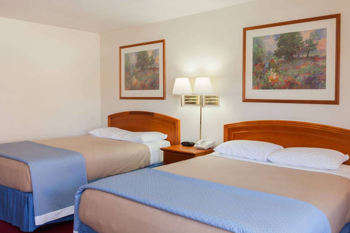 Ein Hotelzimmer mit zwei Betten, einem Nachttisch mit Lampe und zwei gerahmten Bildern an den Wänden.