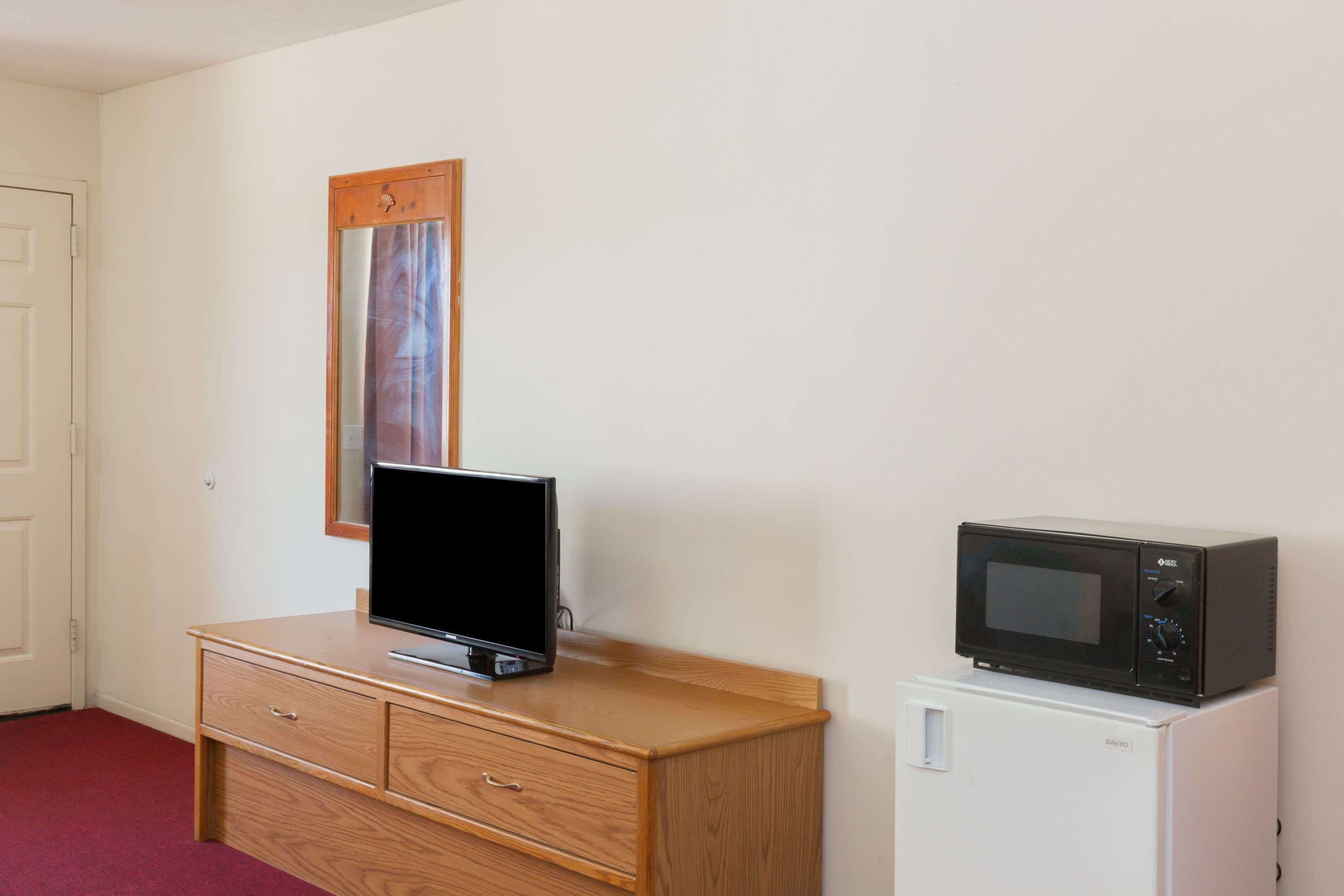 Ein Zimmer mit einem hölzernen Schminktisch, einem Fernseher darauf und einer Mikrowelle auf einem kleinen weißen Gerät.