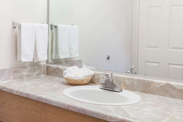 A bathroom with a marble countertop, a sink, a mirror, and two white towels hanging on a towel rack. - Days Inn by Wyndham Castaic Six Flags Magic Mountain (Castaic)