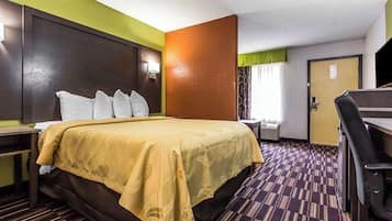 A hotel room with a large bed, a desk, and a chair.