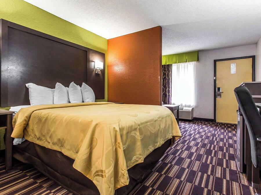 A hotel room with a large bed, a desk, and a chair.