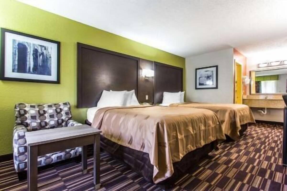 Habitación de hotel con dos camas, un escritorio y una silla. En la pared hay cuadros enmarcados.