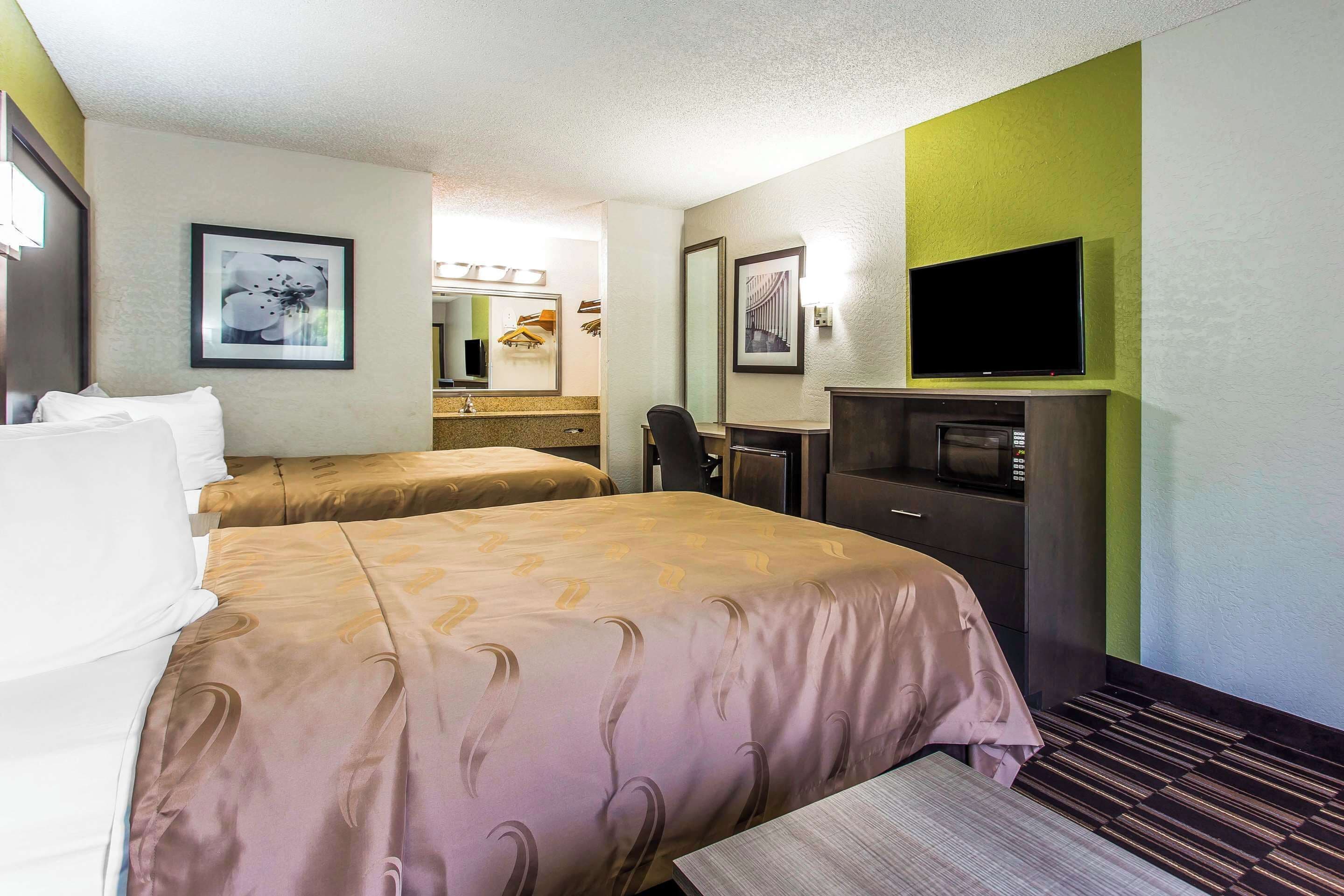 Ett hotellrum med två sängar, ett skrivbord, en tv och ett badrum som syns i bakgrunden.