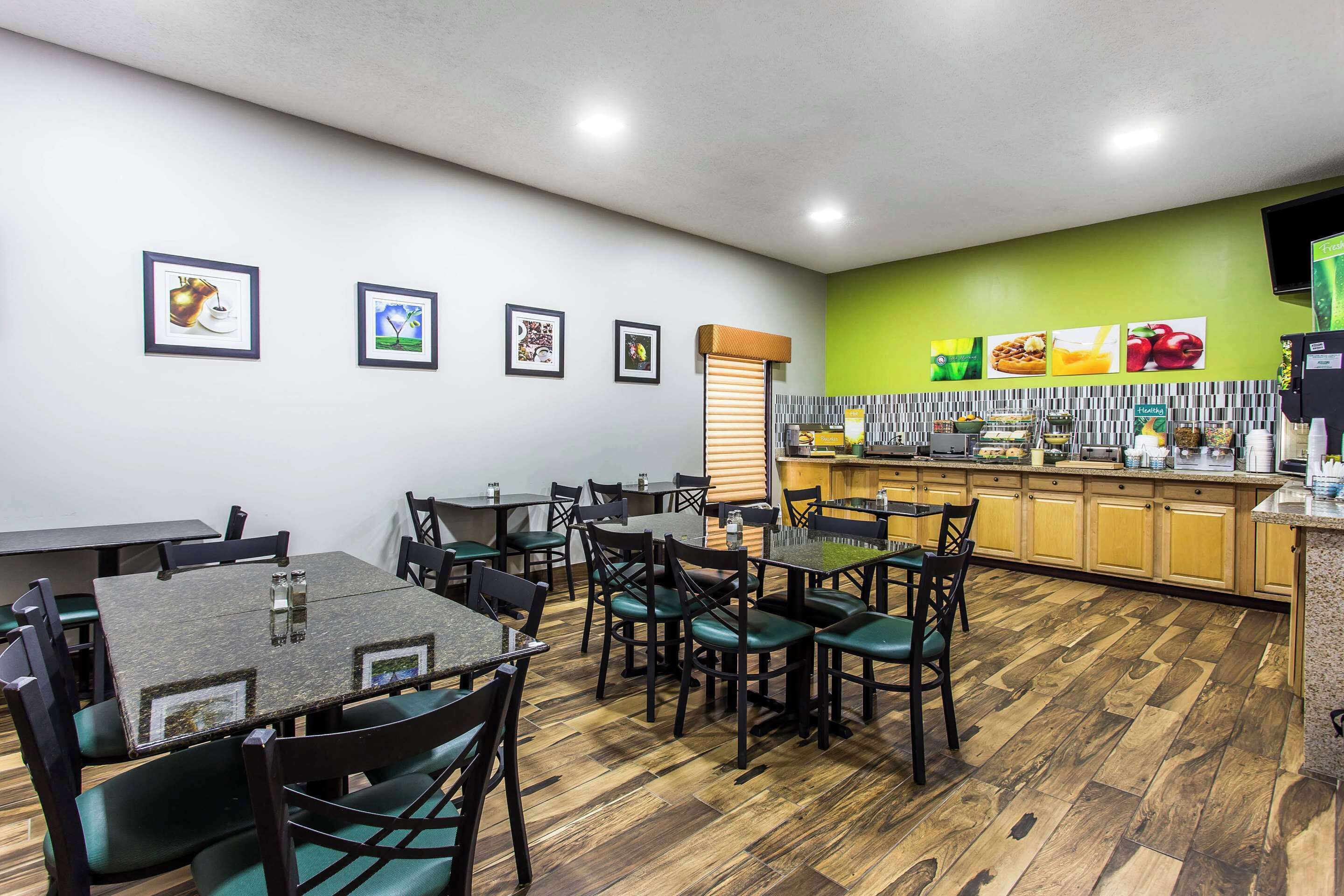 A restaurant with wooden flooring, green chairs, and a counter with food displays.