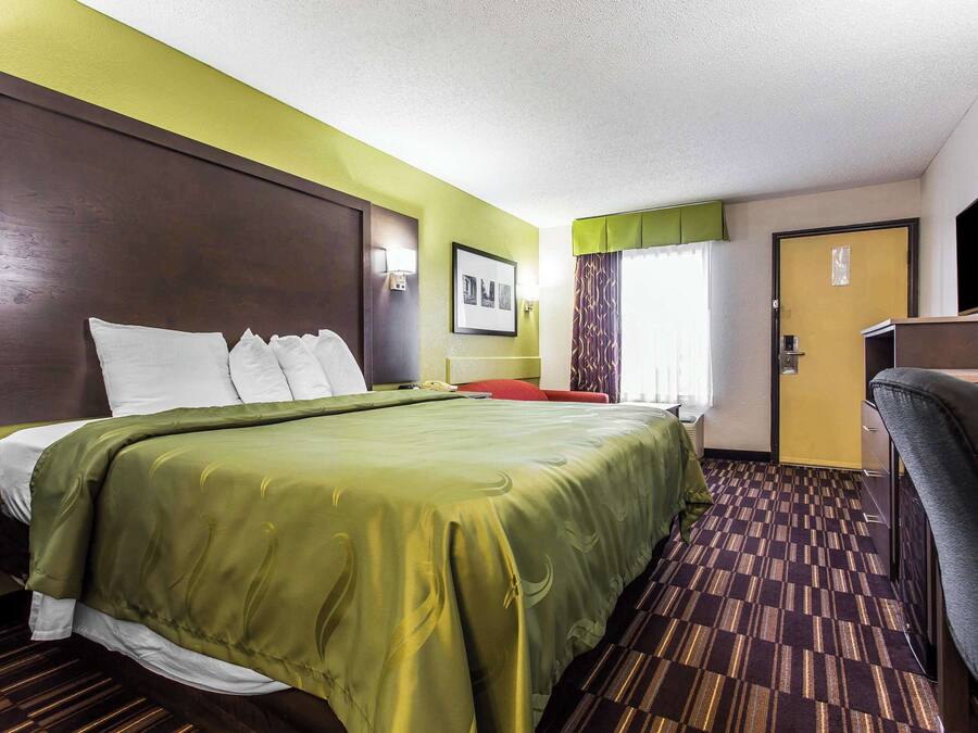 Una habitación de hotel con una cama grande, un escritorio, una silla, un televisor y una puerta.